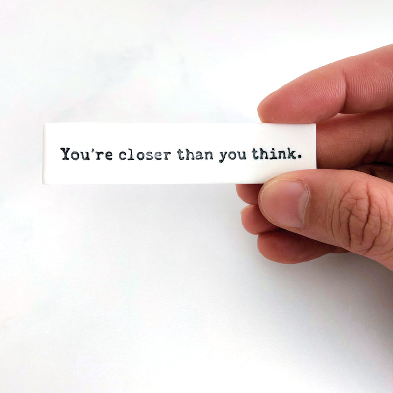 A white Fortune Slip reading “You’re closer than you think.”, held between finger and thumb