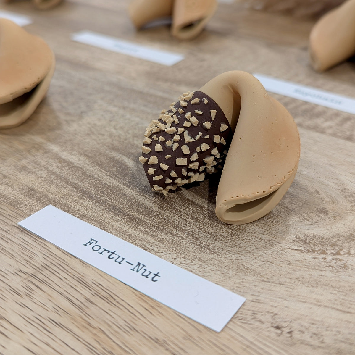 A Fortu-Nut Smart Fortune Cookie, dipped in chocolate and chopped nuts, beside its name card