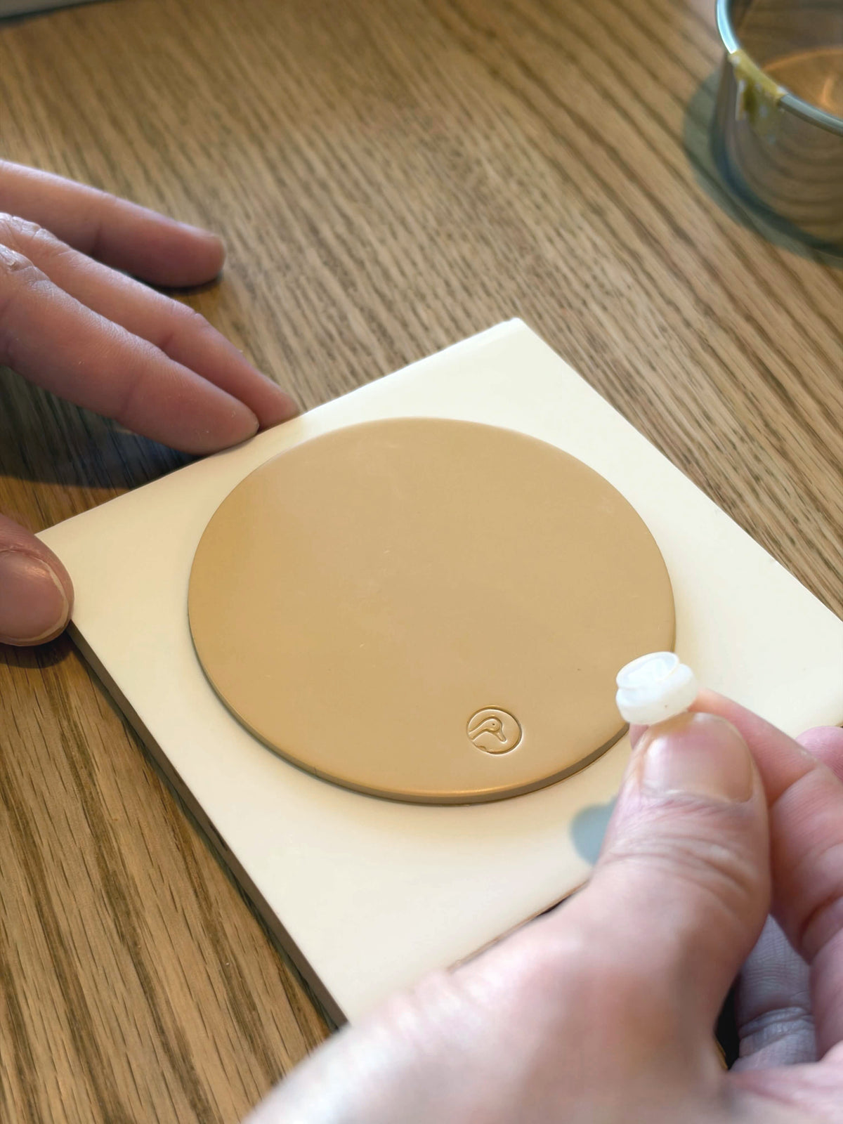 Hands working a flat disc of clay, stamped with the Goose & Pebble mark