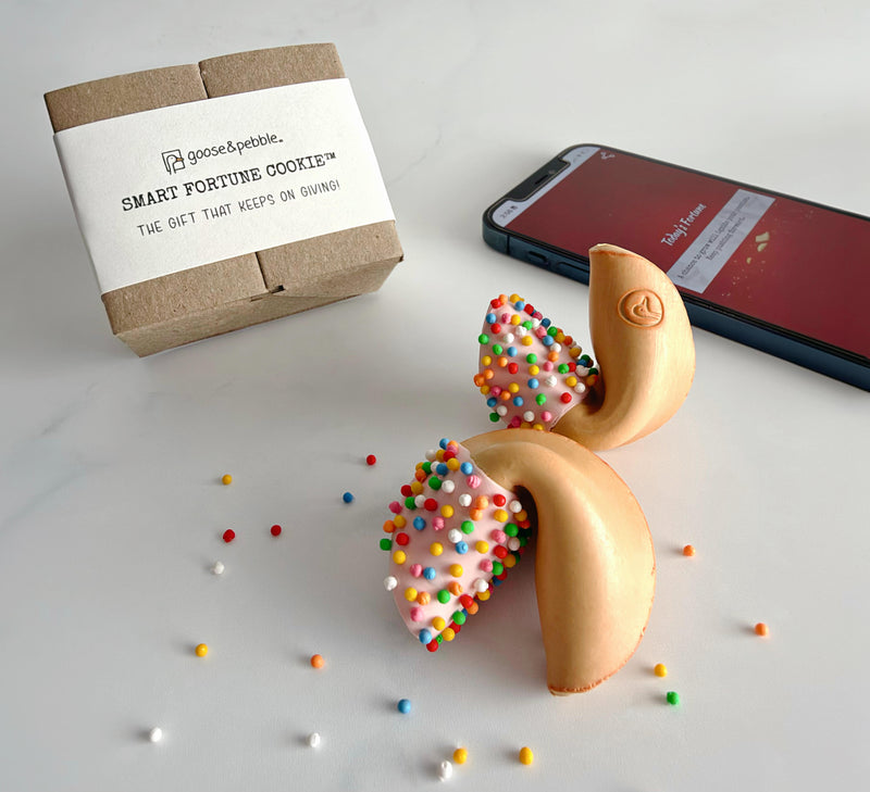 Two 100s & 1000s Smart Fortune Cookies beside their gift box, with a phone showing today's fortune